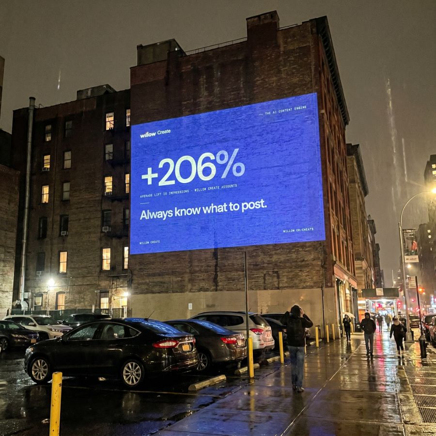 Willow Create projection on a building wall at night reading '+206% — always know what to post.'
